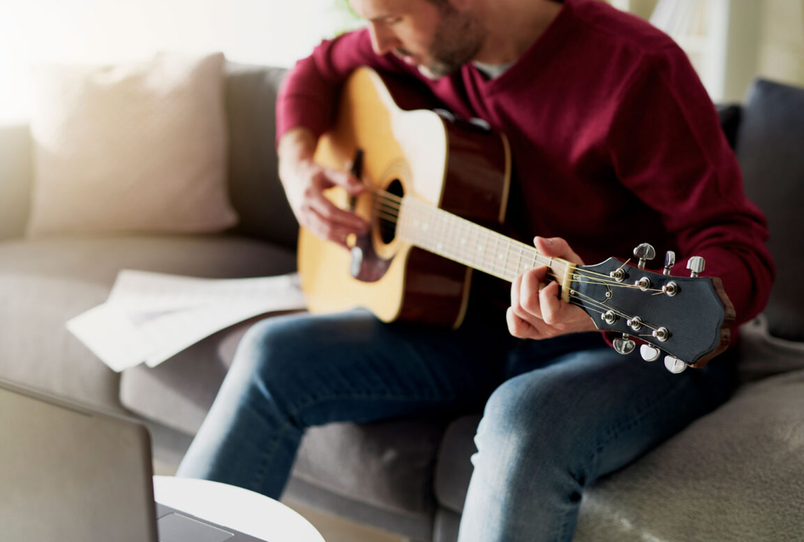 man practicing acoustic guitar on a couch
