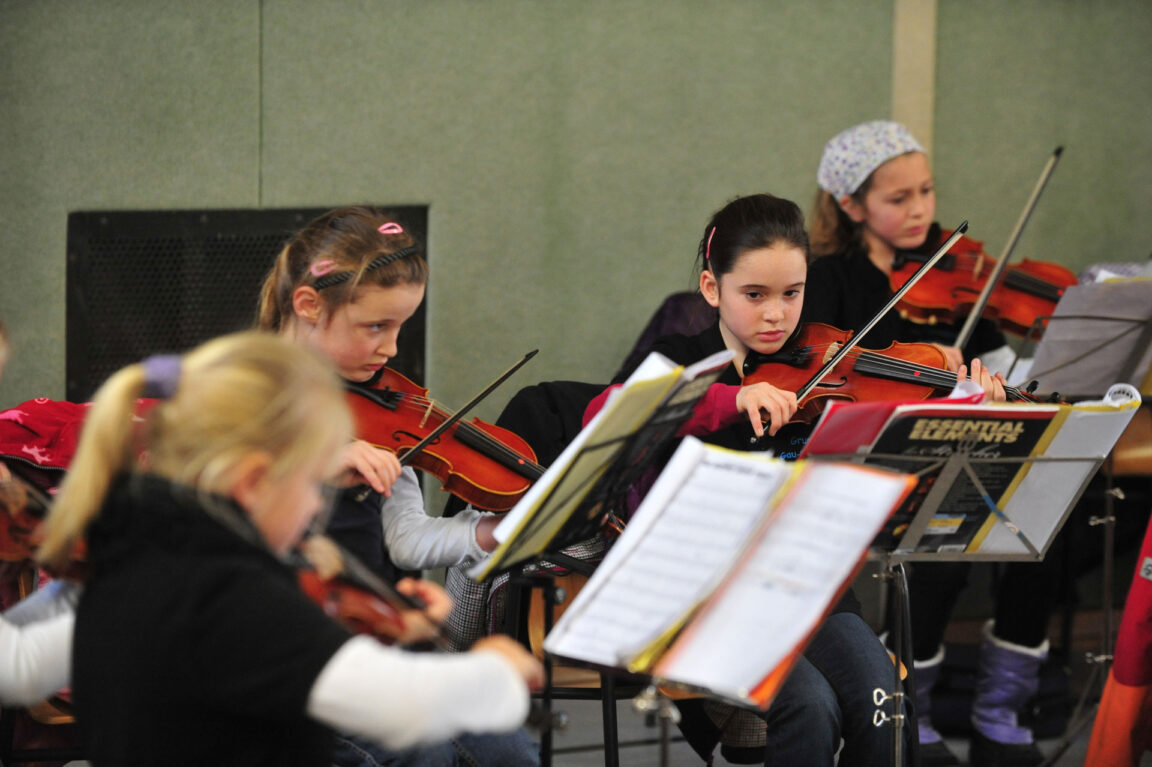 school girls playing violin in orchestra
