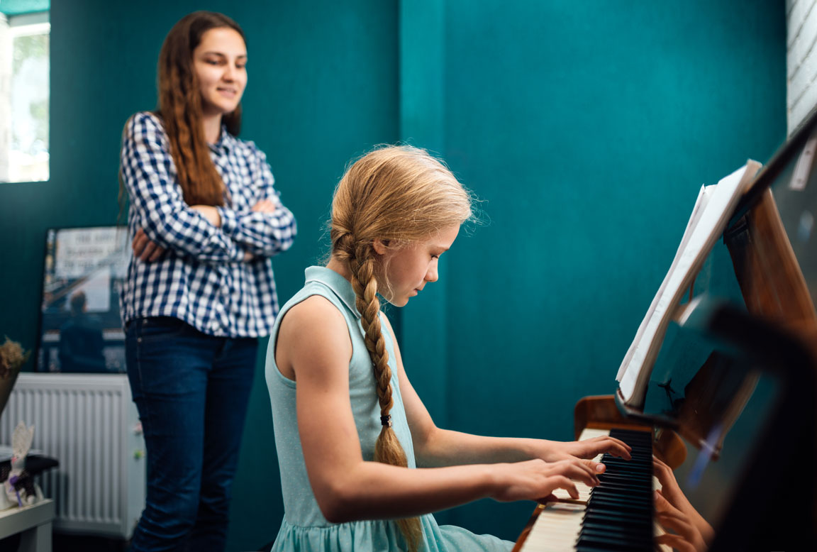 female music teacher watching a young female student play piano
