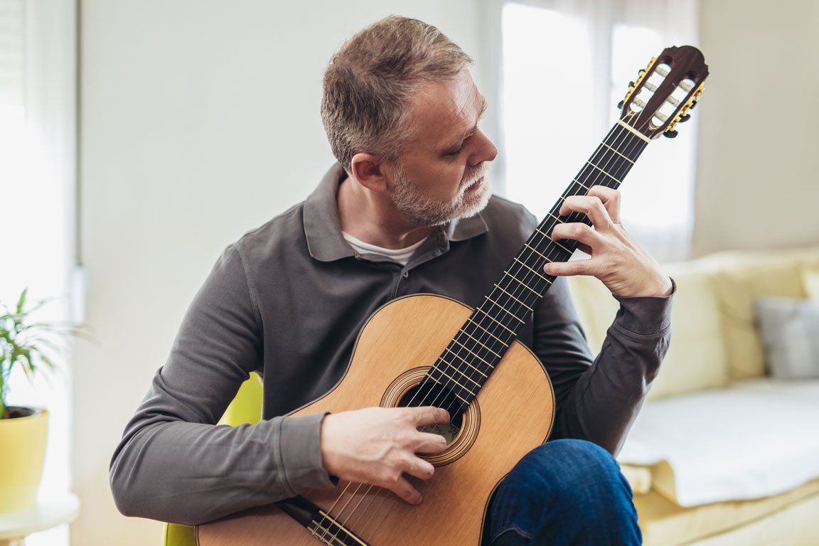 older man with a beard playing classical guitar